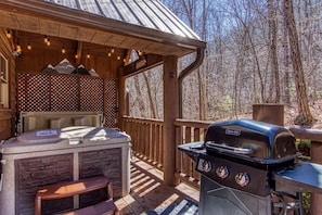 Una terraza al aire libre con una parrilla, un jacuzzi y un pérgola de madera con luces colgantes.