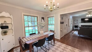 A dining area with a wooden table, chairs, a chandelier, and a view of the outdoors through large windows. - Hilltop Hideaway Near TCU, Dickies Arena & Medical District (Fort Worth)