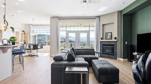 A modern living room with a sectional sofa, a flat-screen TV, and a fireplace. - Beautiful Mountain & Lake Views/UpperLevel Home/King Bed/BBQ/35 min to Big White (Kelowna)
