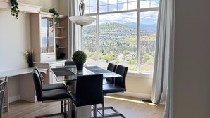 A modern kitchen with a dining area, large windows, and a view of a landscape. - Beautiful Mountain & Lake Views/Upper Level Home/King Bed/BBQ/Sleeps 5 (Kelowna)