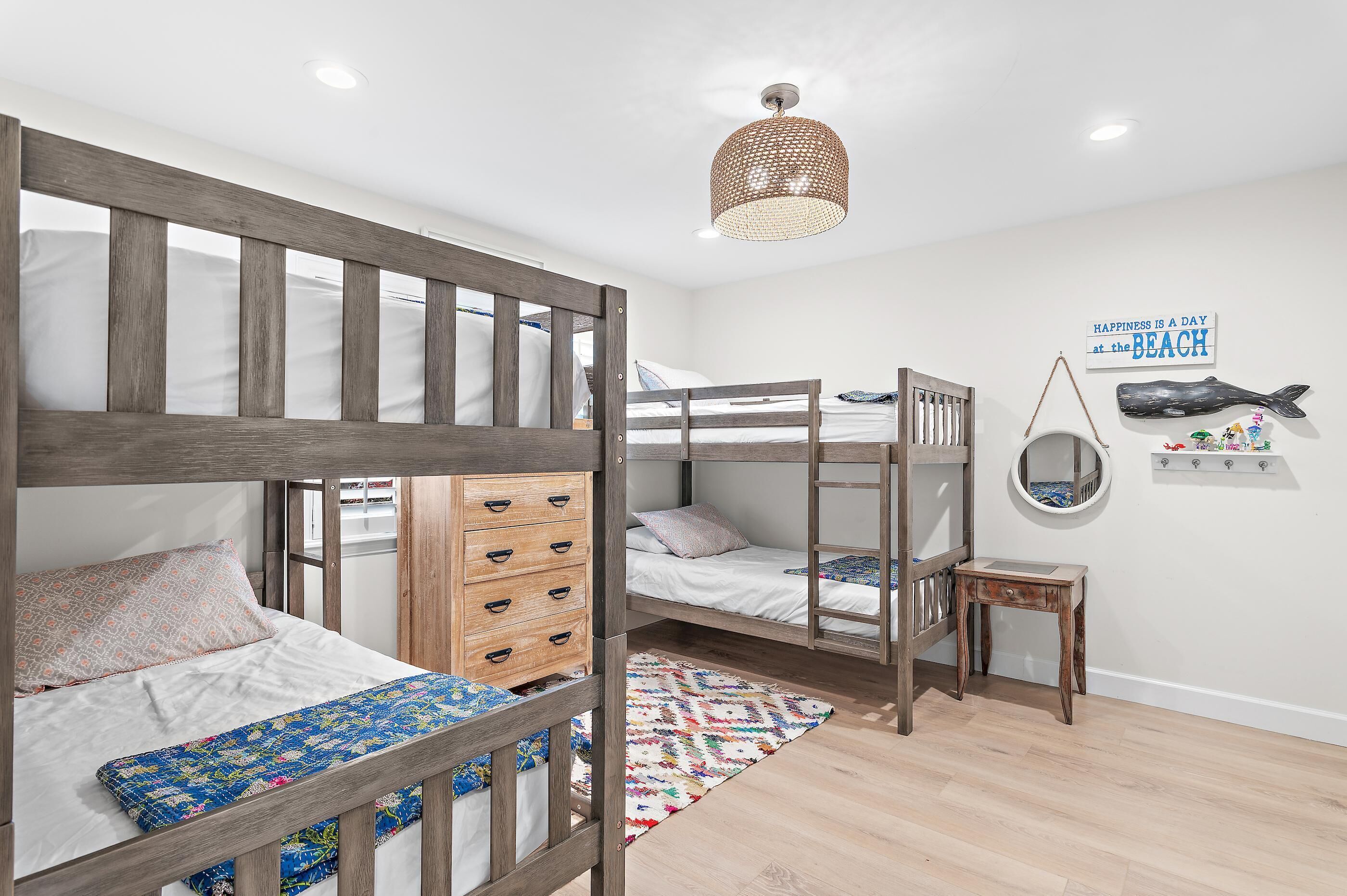 A bunk bed room with a wooden headboard, a small wooden dresser, a round mirror, and a wall-mounted shelf with decorative items.