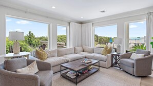 A spacious living area with a large sectional sofa, a coffee table, and multiple windows offering a view of greenery and a blue sky. - Palms of Dune Allen 104 (Santa Rosa Beach)