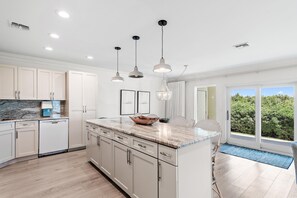 A modern kitchen with white cabinetry, a marble countertop, pendant lighting, and a view through large sliding doors to a balcony. - Palms of Dune Allen 104 (Santa Rosa Beach)