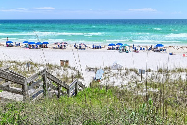 A beach with blue umbrellas, a wooden boardwalk, and a sandy shore. - Palms of Dune Allen 104 (Santa Rosa Beach)