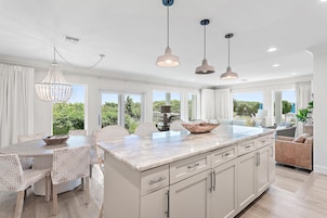 A modern kitchen with a marble countertop, white cabinetry, and pendant lighting.