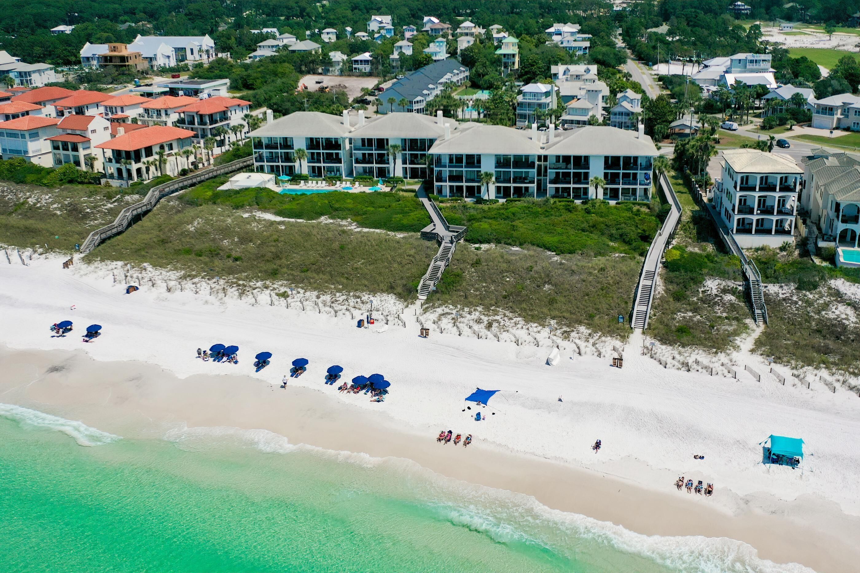An aerial view of a coastal hotel with multiple buildings, a beach with umbrellas, and a boardwalk.