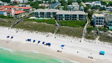 An aerial view of a coastal hotel with multiple buildings, a beach with umbrellas, and a boardwalk.