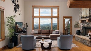 A living room with a large window, a fireplace, and a view of the mountains. - Log Home w/ Epic Views, Hot Tub | Starfall Summit (Steamboat Springs)