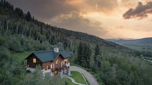 A log cabin with a deck, surrounded by forest, with a view of distant mountains. - Log Home w/ Epic Views, Hot Tub | Starfall Summit (Steamboat Springs)