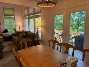 A cozy living room with a wooden table and chairs, a sofa with cushions, a lamp, and a view of a deck through a glass door. - Four Seasons Retreat Hot Tub/Game Room/Ski/Swim (Lake Harmony)