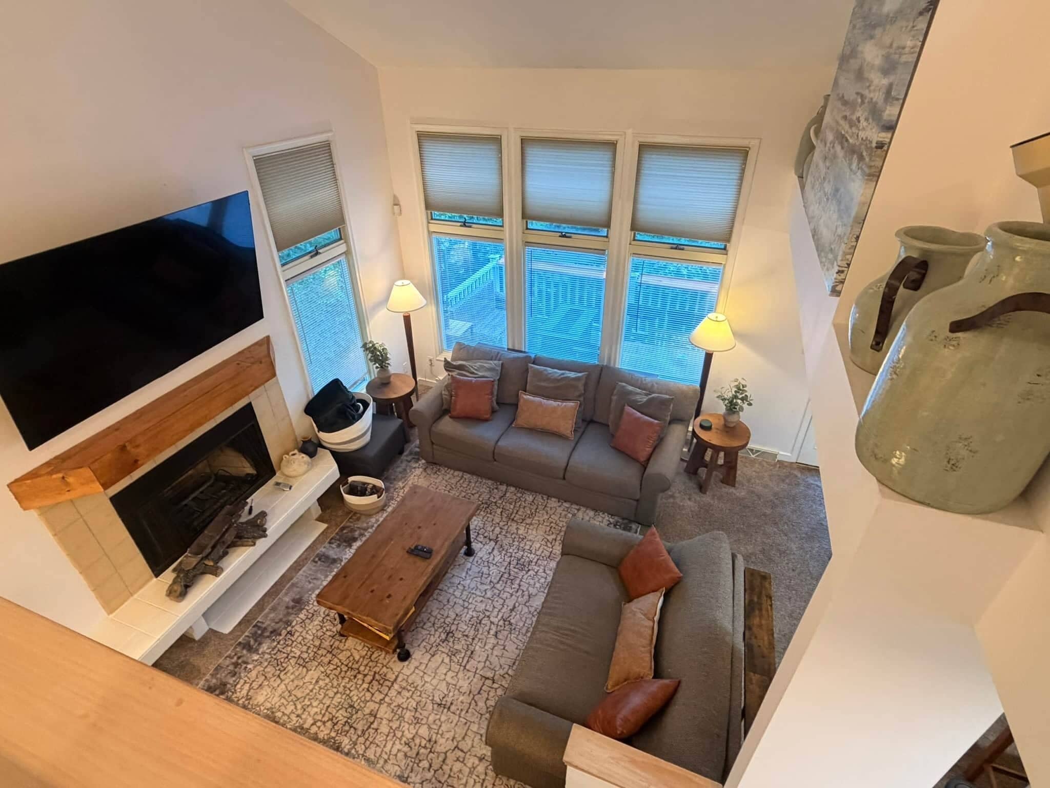 Een woonkamer met een open haard, bank, salontafel, televisie en grote ramen.