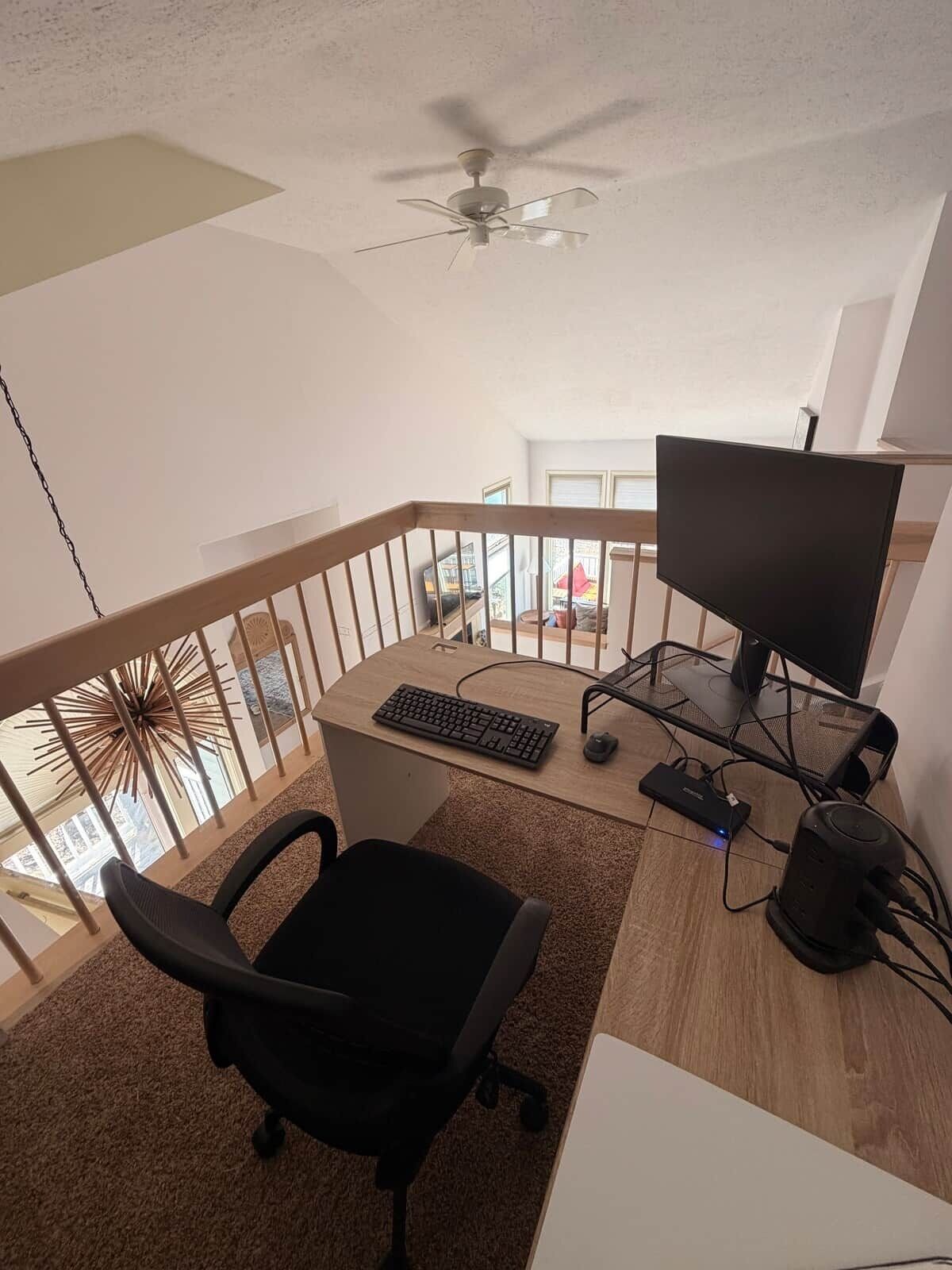 A balcony with a ceiling fan, a desk with a computer setup, and a chair.
