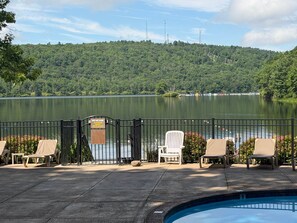 A pool area with chairs and a sign, a lake, and a forested hill in the background. - Four Seasons Retreat Hot Tub/Game Room/Ski/Swim (Lake Harmony)
