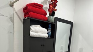 A bathroom with a toilet, a sink, a mirror, a shelf with towels, and a vase with flowers. - Private Cozy Studio (Sunrise)