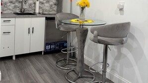 A modern kitchen with white cabinets, a marble backsplash, a microwave, and a glass table with a vase of yellow flowers. - Private Cozy Studio (Sunrise)
