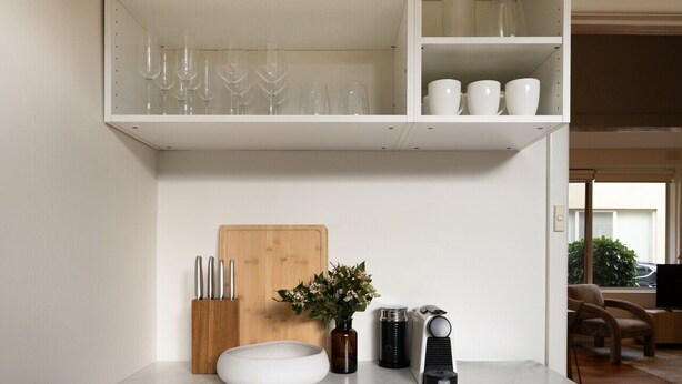 Eine Küche mit weißen Schränken, einem Holztisch zum Schneiden, einer Kaffeemaschine und einer Vase mit Blumen.