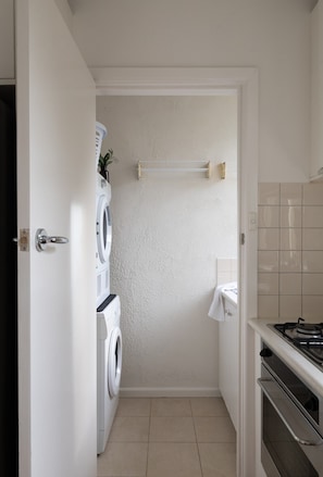 A compact laundry room with a washing machine, a drying rack, and a sink. - Beautifully Styled Apartment in St Kilda East (Saint Kilda East)