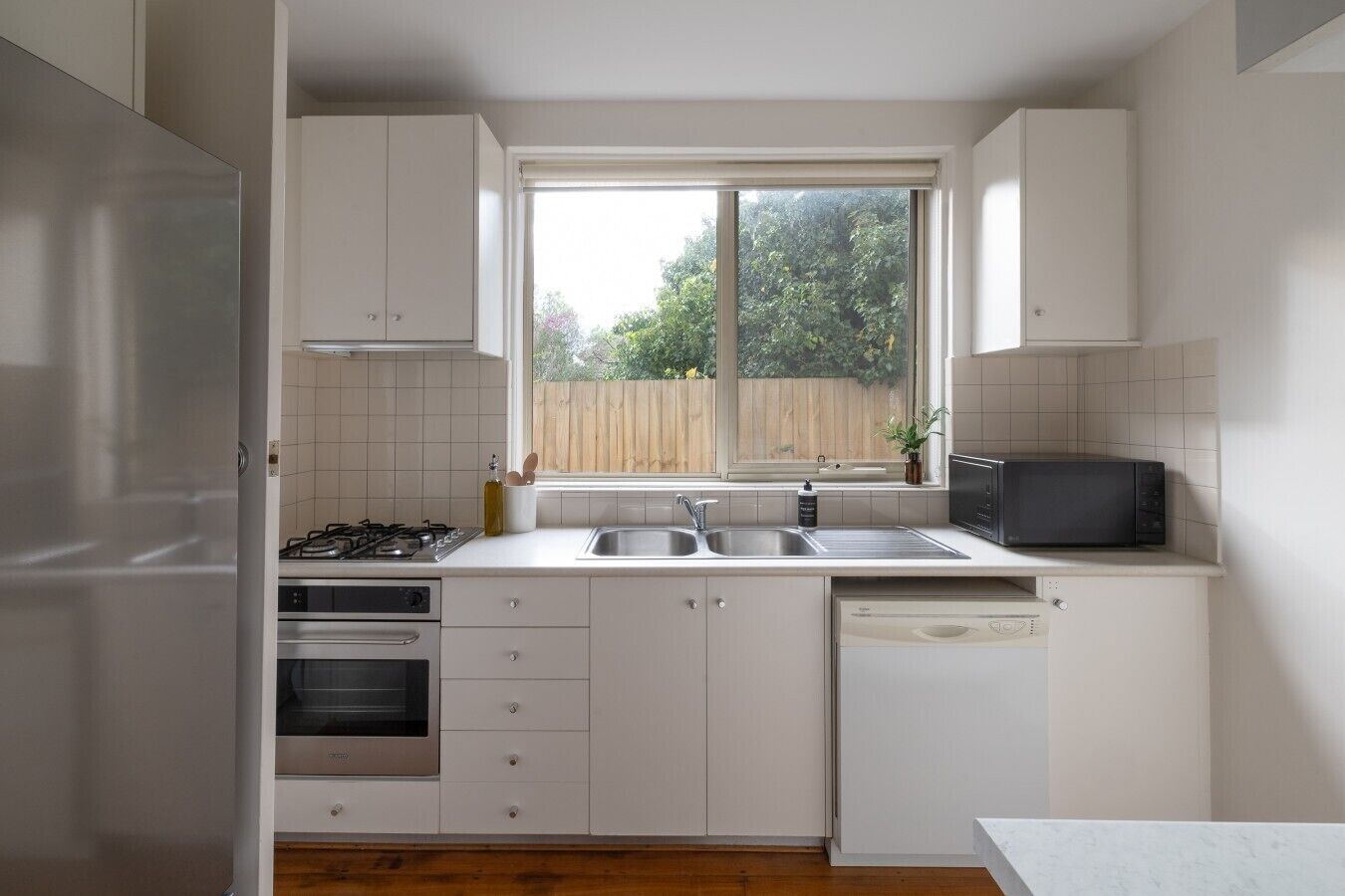 Une cuisine de taille réduite avec des meubles blancs, une cuisinière à gaz, un four à micro-ondes et un évier.