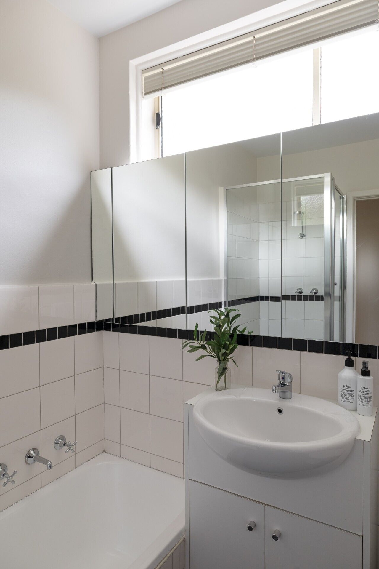 Une salle de bain moderne avec un lavabo blanc, une douche à parois de verre et un grand miroir au-dessus du lavabo.