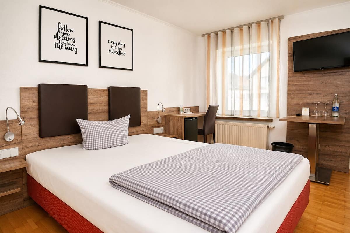 A hotel room with a bed, a desk, a chair, a TV, and two motivational posters on the wall.