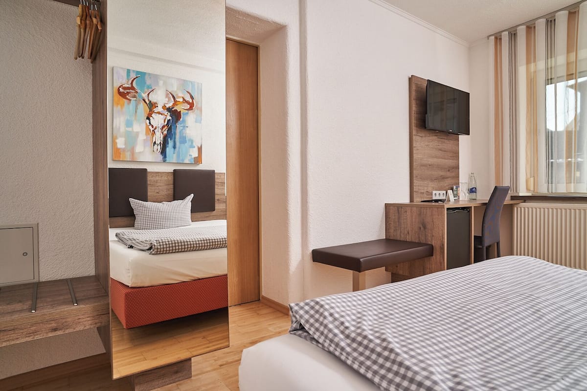 A hotel room with a bed, a desk, a TV, and a painting on the wall.