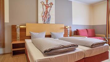 Quarto de hotel com duas camas, uma cabeceira de madeira, uma obra de arte na parede e um sofá vermelho.