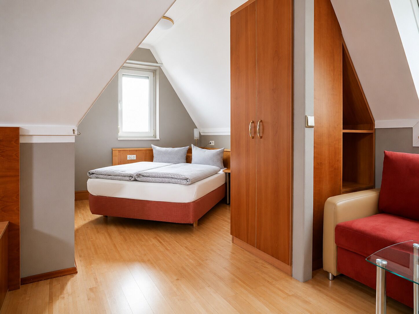 Un dormitorio con cama, armario de madera y una silla roja.