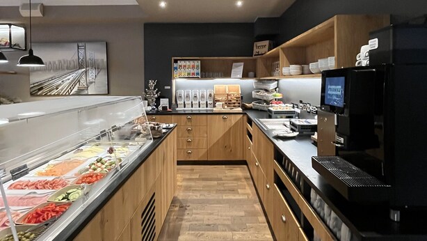 Une cuisine moderne avec des meubles en bois, un présentoir en verre contenant des produits alimentaires, une machine à café et un téléviseur.