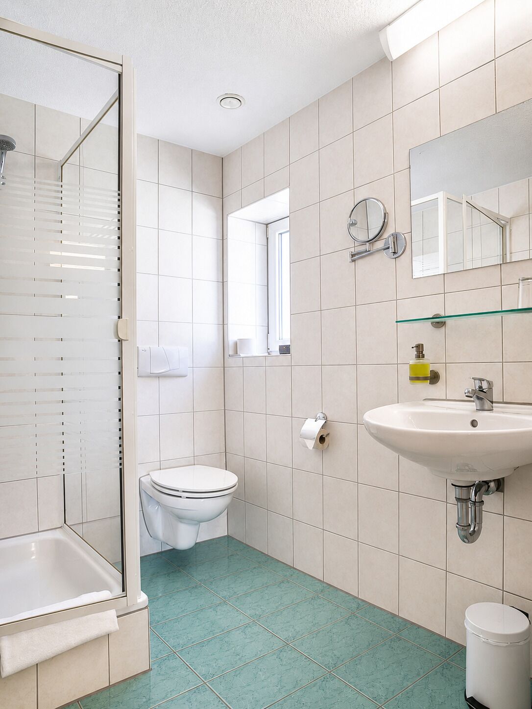Un baño con cabina de ducha de vidrio, inodoro, lavabo con espejo y ventana.