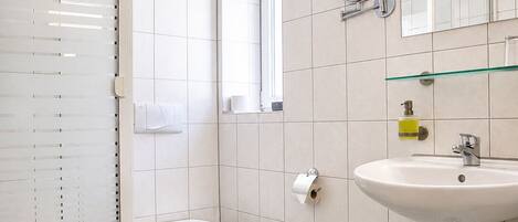 Un baño con cabina de ducha de vidrio, inodoro, lavabo con espejo y ventana.