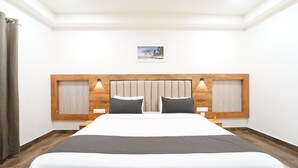 Habitación de hotel con una cama grande, cabecera de madera, dos lámparas de noche, una mesita de noche y un cuadro en la pared.