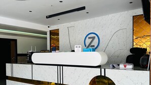 Una moderna recepción con un diseño de mármol, un gran letrero iluminado con la letra 'Z' y un espejo circular dorado.