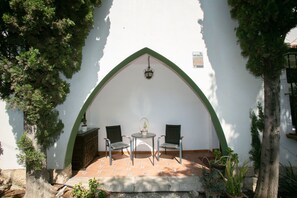 Un patio con una mesa y sillas, rodeado por un muro blanco con un arco verde.