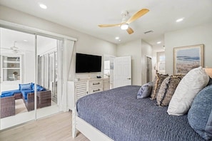 Ein Schlafzimmer mit einem Bett, einem Fernseher, einem Deckenventilator und einer Glastür, die auf einen Balkon führt.