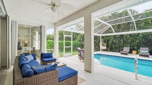 Un'area esterna moderna con piscina, mobili in rattan e ventilatore a soffitto.