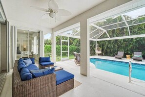 Ein moderner Außenbereich mit Pool, Korbmöbeln und Deckenventilator.