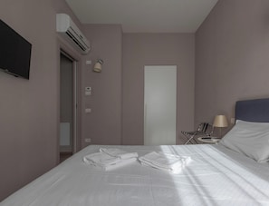 Una habitación de hotel con cama, mesita de noche con lámpara, aire acondicionado y una puerta.