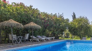 A swimming pool with lounge chairs and thatched umbrellas, surrounded by lush greenery. - Holiday Home 'El Mimbral' with Shared Pool, Wi-Fi and Air Conditioning (Vejer de la Frontera)