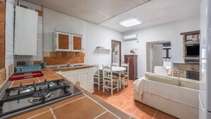 A compact kitchen with a gas stove, white cabinets, a dining table with chairs, and a sofa. - Holiday Home 'El Mimbral' with Shared Pool, Wi-Fi and Air Conditioning (Vejer de la Frontera)