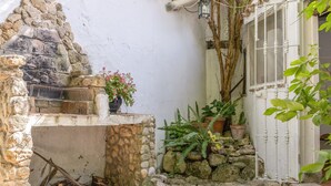 A stone-built outdoor area with a rustic fire pit, potted plants, and a white gate. - Holiday Home 'El Mimbral' with Shared Pool, Wi-Fi and Air Conditioning (Vejer de la Frontera)