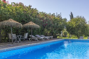 A swimming pool with lounge chairs and thatched umbrellas, surrounded by lush greenery. - Holiday Home 'El Fresno' with Shared Pool, Wi-Fi and Air Conditioning (Vejer de la Frontera)