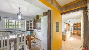 Una cocina con armarios blancos, una mesa de comedor con sillas, un refrigerador y una ventana con vistas a zonas verdes.