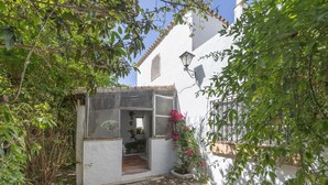 Un patio estrecho con un edificio blanco, una zona pequeña cubierta con plantas y un camino de piedra.