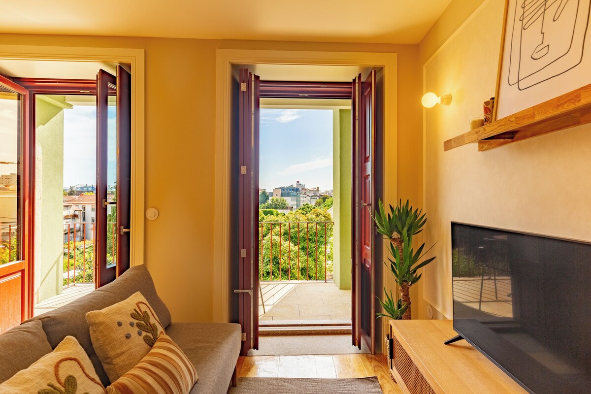 Quarto com sofá, televisão e varanda com vista para a cidade.