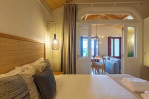 Une chambre d’hôtel avec un lit, une tête de lit, une table de chevet, une lampe et une vue sur un espace de restauration, visible à travers une porte ouverte.