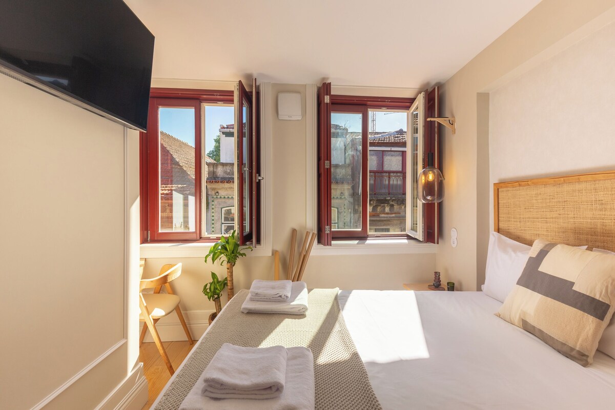 Um quarto com uma cama, televisão, janela, cadeira e planta.
