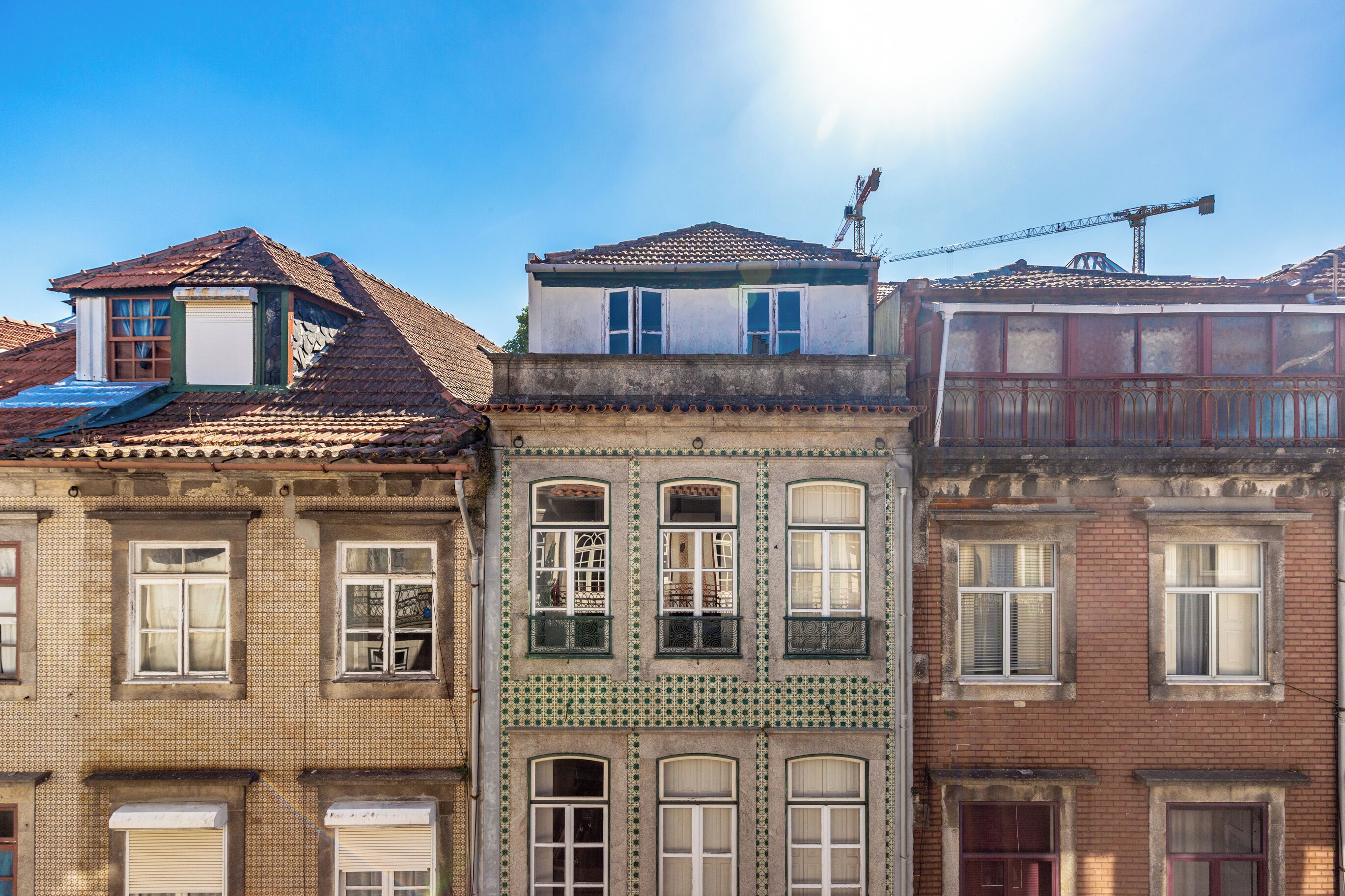 Een rij gebouwen met drie verdiepingen en verschillende architectuurstijlen, waaronder een balkon en een kraan op de achtergrond.