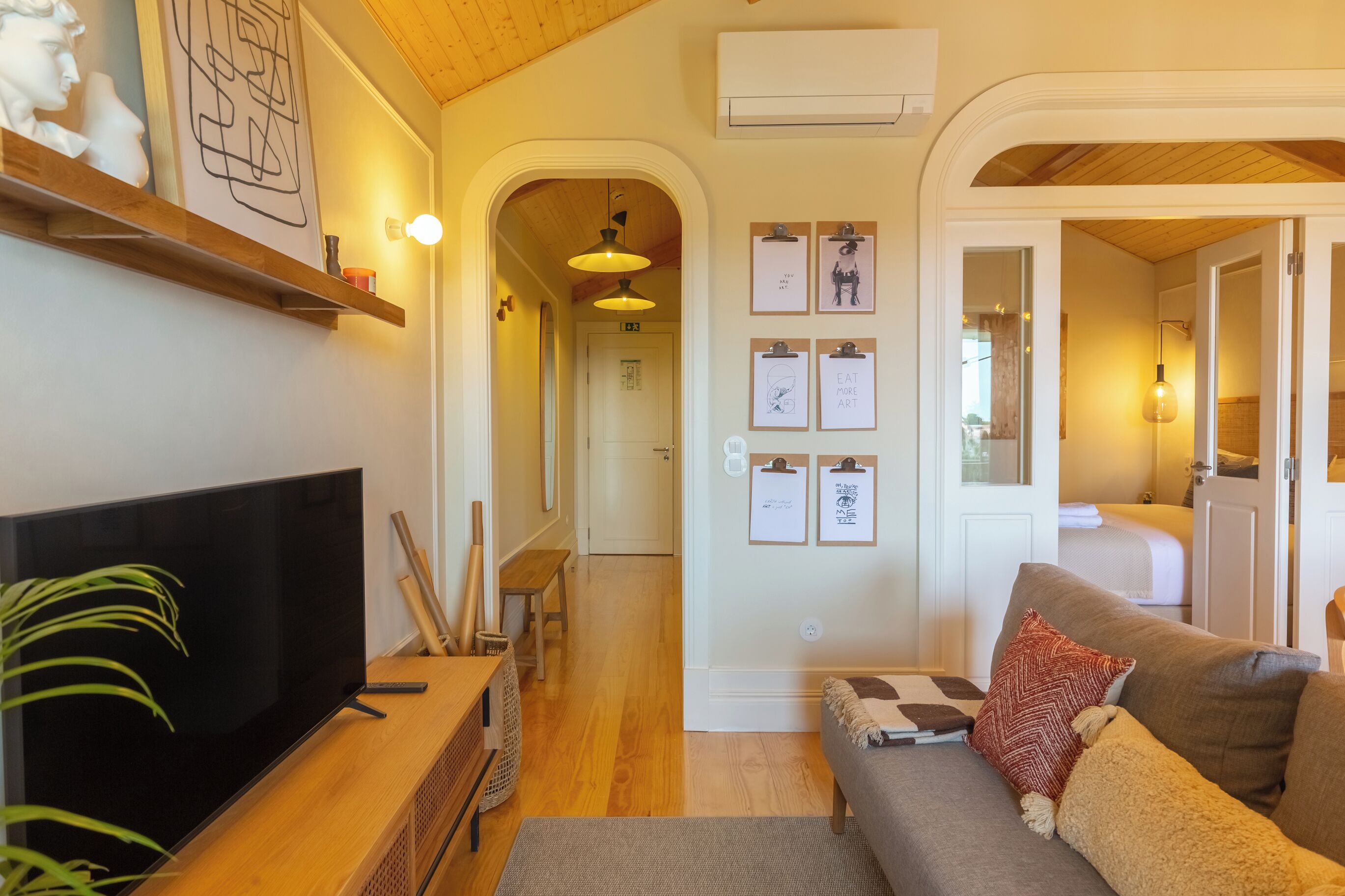 A living room with a TV, wooden furniture, a sofa, and a hallway leading to a bedroom.