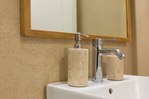 Un lavabo de bany amb un mirall, un dosificador de sabó i un aixeta.