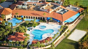Ein Resort mit mehreren Schwimmbecken, Palmen und einem Tennisplatz.